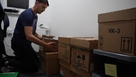 a young man stacks cardboard boxes in a room ready for the move and nods happily