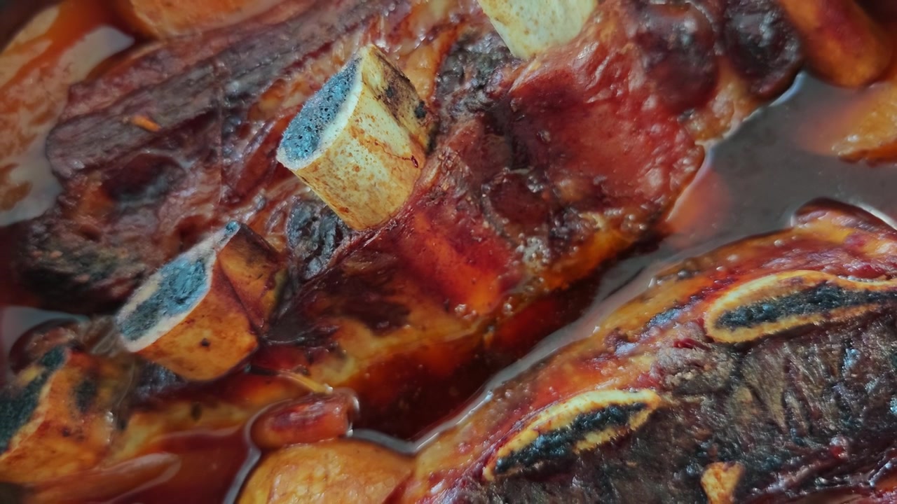 Vista dall'alto di costine di manzo Asado a cottura lenta in brodo ricco con patate, patate dolci e cipolla che bollono in una pentola nera. Stufato di carne gourmet rustico, primo piano di comfort food.