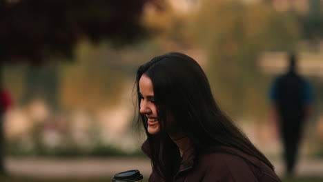 beautiful cheerful joyful brunette girl model laughing and holding coffee cup in outdoor park, blurred background