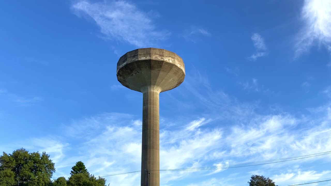 Tall, slim and old brown coloured stone water tower storage structure under a clear blue sky.Slow Tilting up.