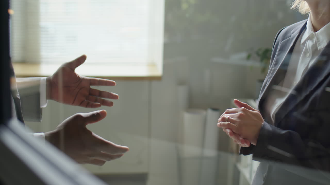 Colleghi che si stringono la mano e parlano dietro la parete di vetro dell'ufficio