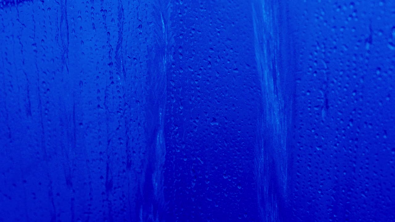 Primer plano de agua fluyendo y gotas resbalando por un cristal mojado con fondo azul. Concepto de lluvia, ambiente melancólico, textura abstracta y componentes visuales de clima o meteorología