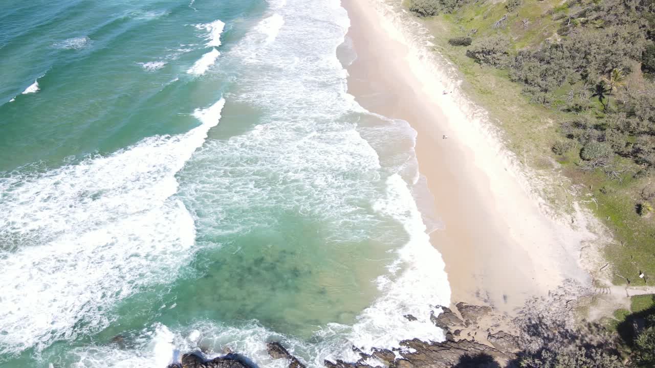 Aerial drone pans up to showcase blue water and sandy beach in Noosa on sunny day