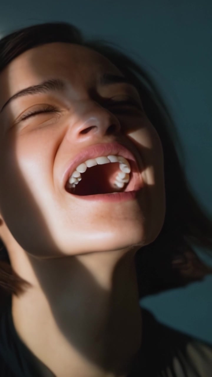 A woman experiencing raw, unfiltered joy as she laughs heartily in soft light, capturing an authentic moment of happiness and emotional expression through laughter.