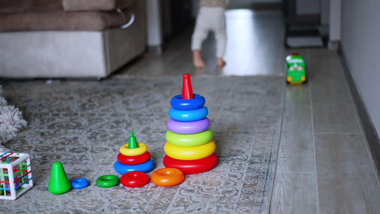 Little kid crawls away from toys on the floor. Baby leaves his pyramids, then stands up and runs away. Blurred backdrop.