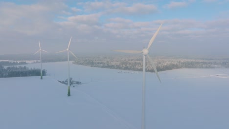 Vista-Aérea-De-Turbinas-Eólicas-Que-Generan-Energía-Renovable-En-El-Parque-Eólico,-Paisaje-De-Campo-Lleno-De-Nieve-Con-Niebla,-Soleada-Noche-De-Invierno-Con-Luz-De-Hora-Dorada,-Amplio-Tiro-De-Drones-Moviéndose-Hacia-Atrás