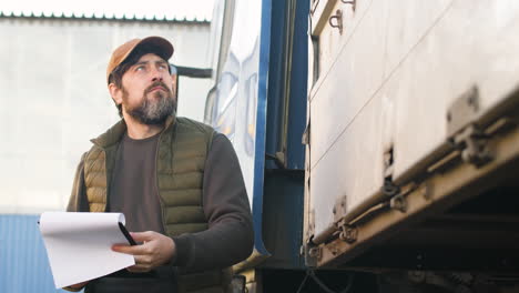 bottom view of worker wearing vest and cap organizing a truck fleet in a logistics park while reading documents