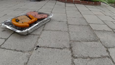 locked off view of disposable mini bbq grill with different meats