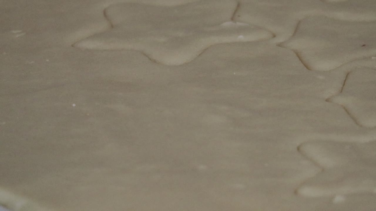 An extreme close up of a gingerbread man shaped cookie cutter being used to cut out a cookie dough shape for Christmas cookies