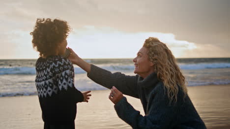 Little-kid-talking-phone-on-ocean-shore.-Happy-mother-giving-smartphone-to-son