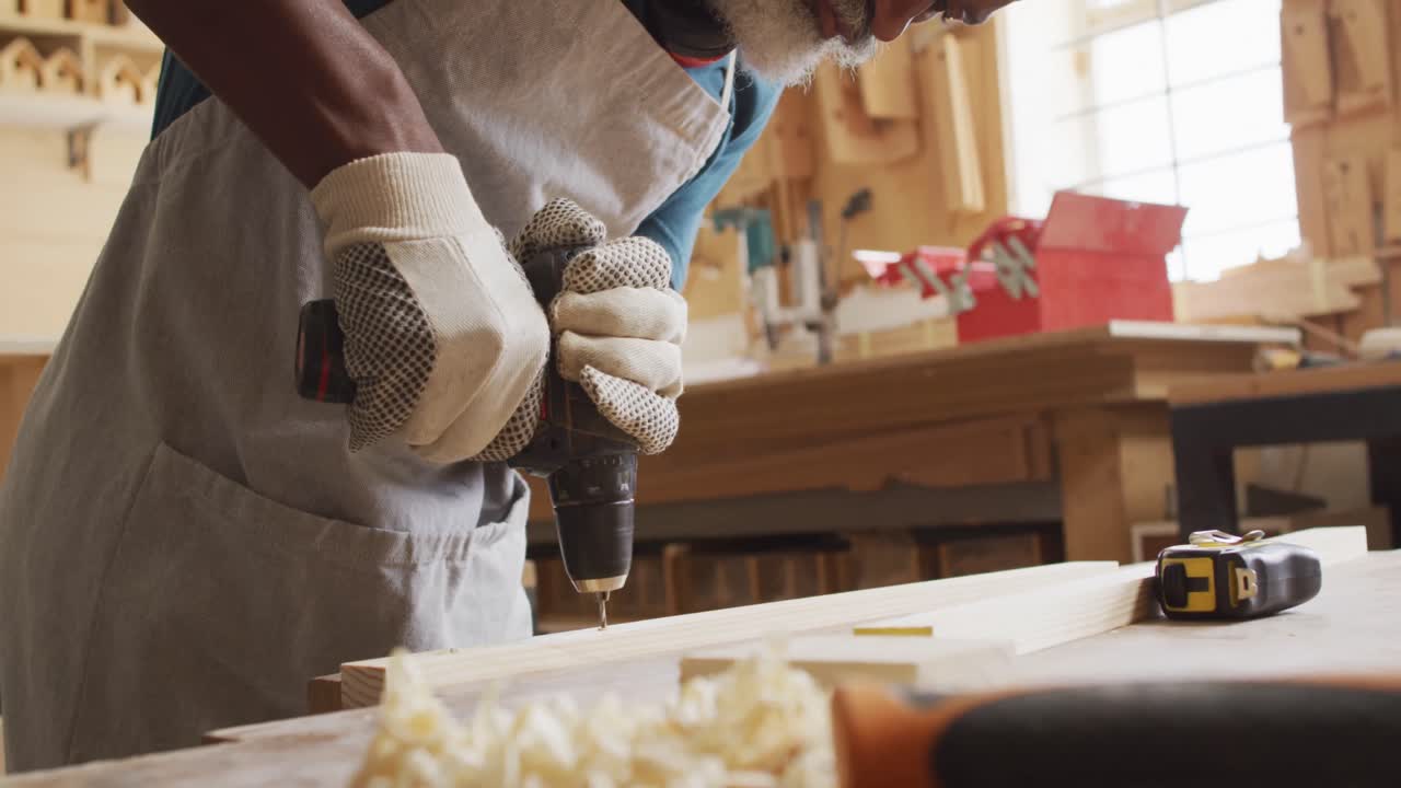 African american male carpenter drilling holes in wooden plank using hand drilling machine