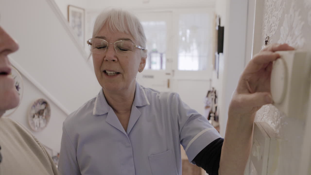A nurse assisting an elderly man with a thermostat at home
