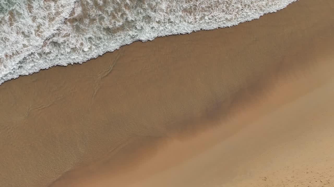 Luftfoto af bølger, der møder sand på en strand