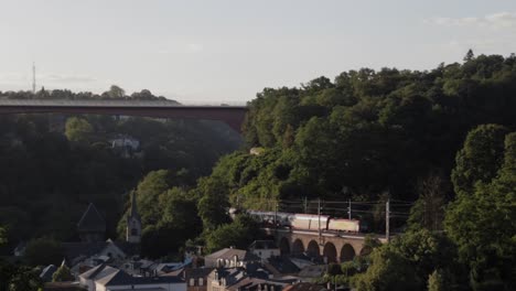 Tren-Conduciendo-A-Lo-Largo-De-La-Meseta-De-Kirchberg-A-Través-Del-Valle-De-Alzette-En-La-Ciudad-De-Luxemburgo-Al-Atardecer-En-Un-Día-De-Verano