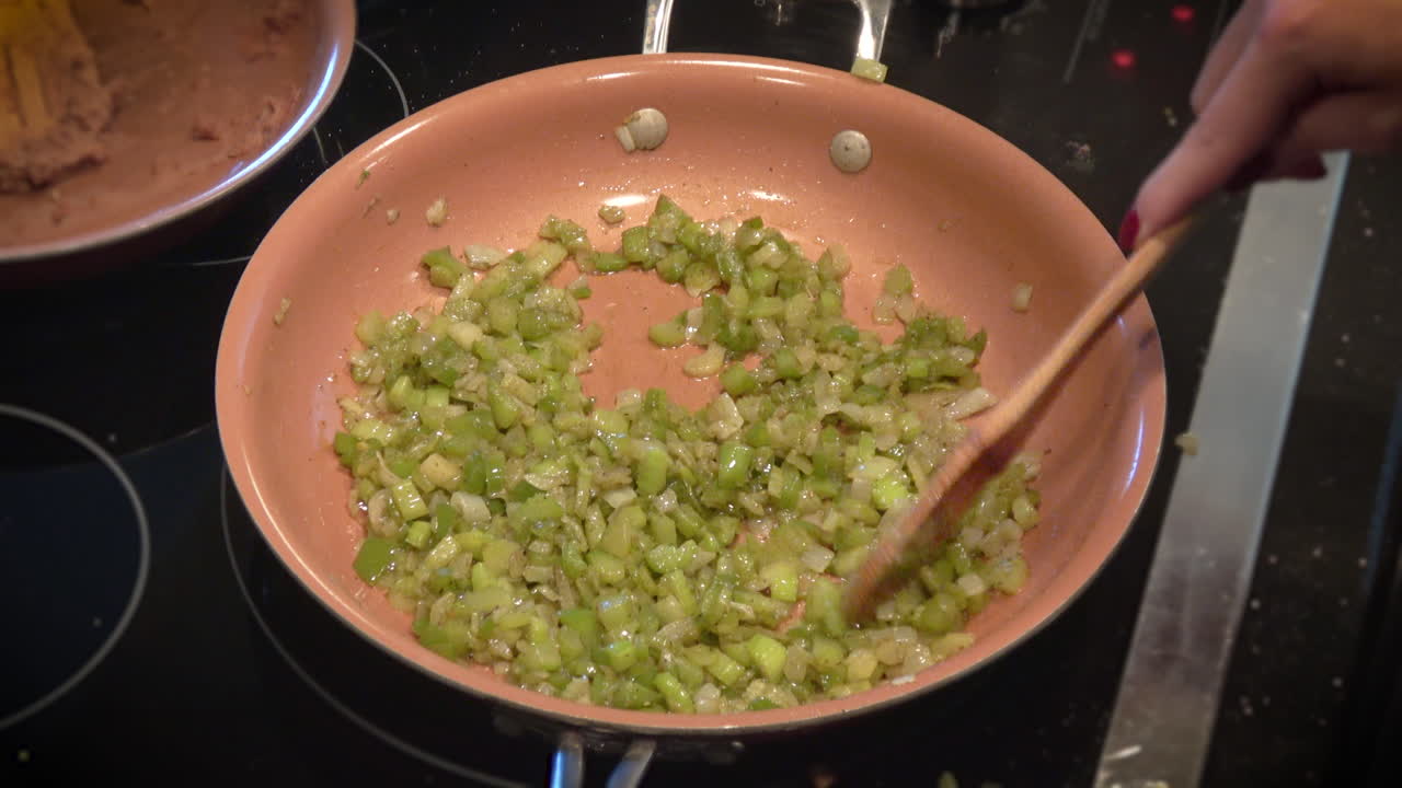 여자는 셀러리와 양파를 인덕션 스토브 위에 볶고, 오버헤드를 닫습니다 -- 4k