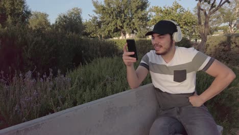 smiling young man, listening music, checks his mobile, in a park