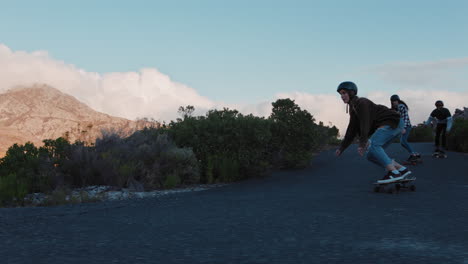 Felices-Amigos-Multiétnicos-Haciendo-Longboard-Juntos-Navegando-Cuesta-Abajo-En-Una-Hermosa-Carretera-Rural-Divirtiéndose-Patinando-Disfrutando-De-Unas-Relajadas-Vacaciones-De-Verano-En-Cámara-Lenta