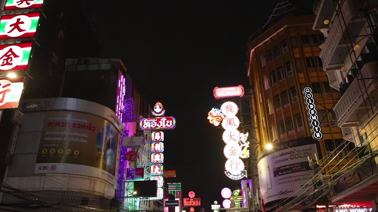 Busy Chinatown street with neon signs, tuk-tuks, cars, and pedestrians at night, handheld camera movement