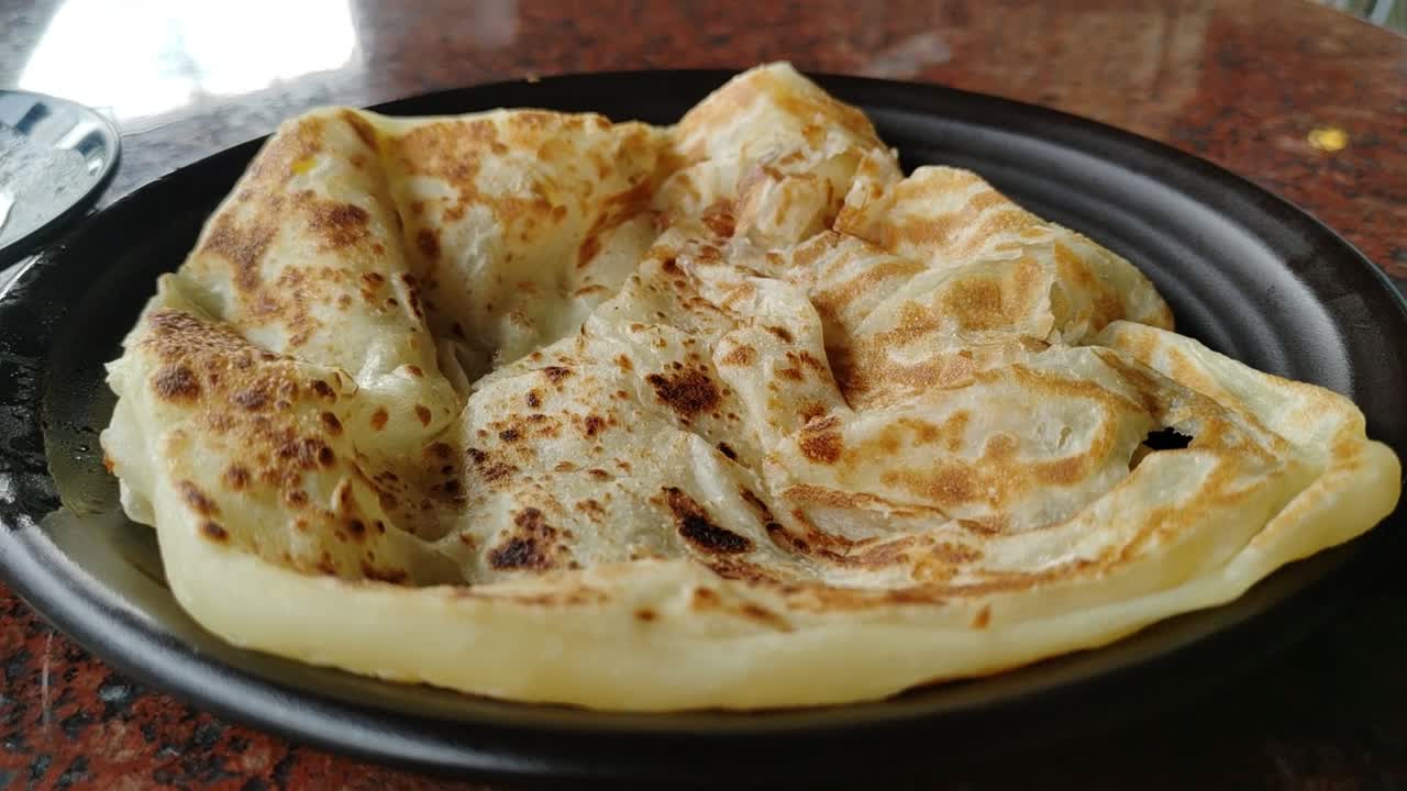 A serving of roti canai, a popular Malaysian dish, placed on a table with a side of dhal curry. A simple and beloved breakfast choice.