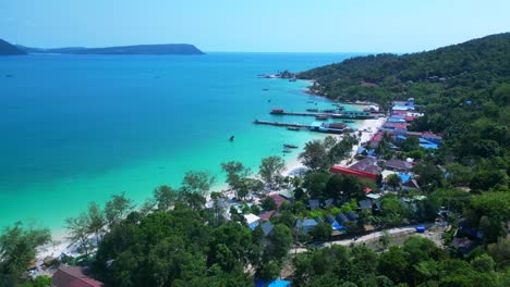 koh rong island with crystal clear turquoise waters, white sandy beach, and a vibrant fishing village nestled along the coastline. dramatic aerial view flight panorama overview drone