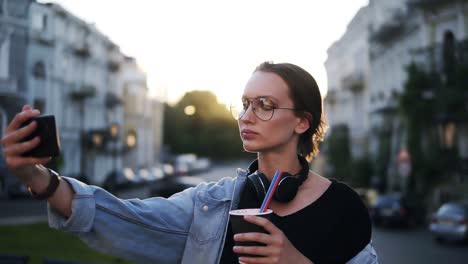 portrait of young attractive woman in sunglasses with headphones on neck posing on the camera in the city street. close up