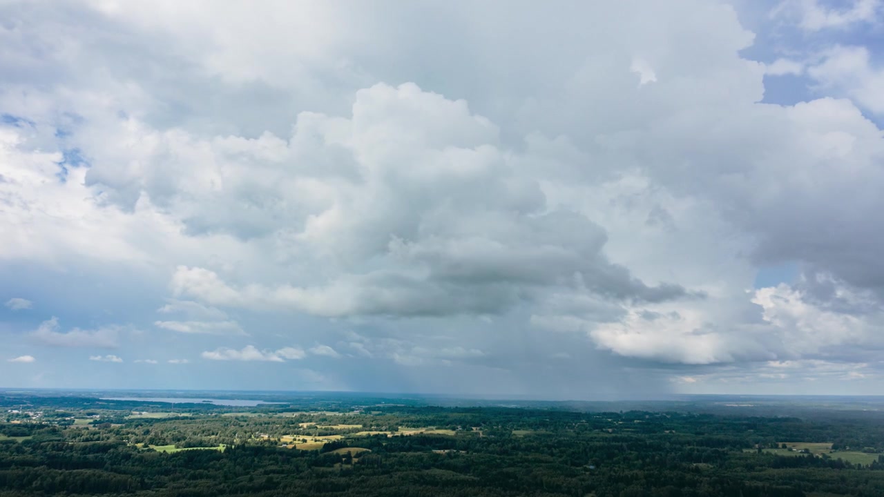 Aerial drone hyperlapse view of dramatic stormy rain clouds moving over a vast green countryside landscape and distant lake.
