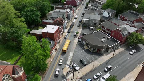 bus driver leaving yellow american school bus on street in american neighborhood. aerial top down shot. green trees in summer. traffic jam on narrow street.