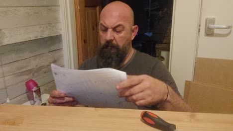 Confused-Caucasian-bearded-male-reading-and-throwing-flat-pack-furniture-instructions-in-frustration