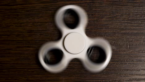 person using a white fidget spinner on a wooden table