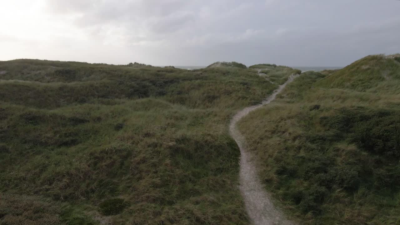 low-altitude drone facing towards the ocean at Hvide Sande, Denmark and slowly moves upwards, revealing the beach and turbulent north sea, capturing the dramatic coastal landscape on stormy day