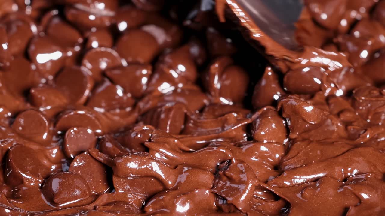 A spoon smoothly blends partially melted chocolate chips, creating a rich and glossy texture.