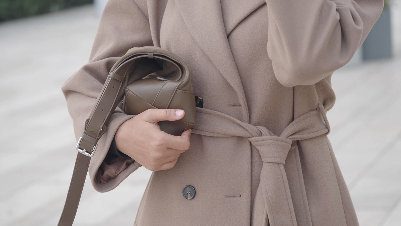 Stylish Woman in Beige Coat Holding a Small Handbag