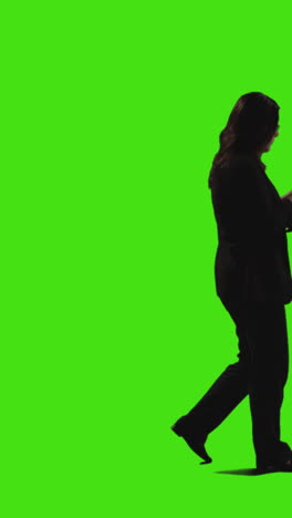 vertical video side view shot of businesswoman text messaging on mobile phone walking across frame against green screen 1