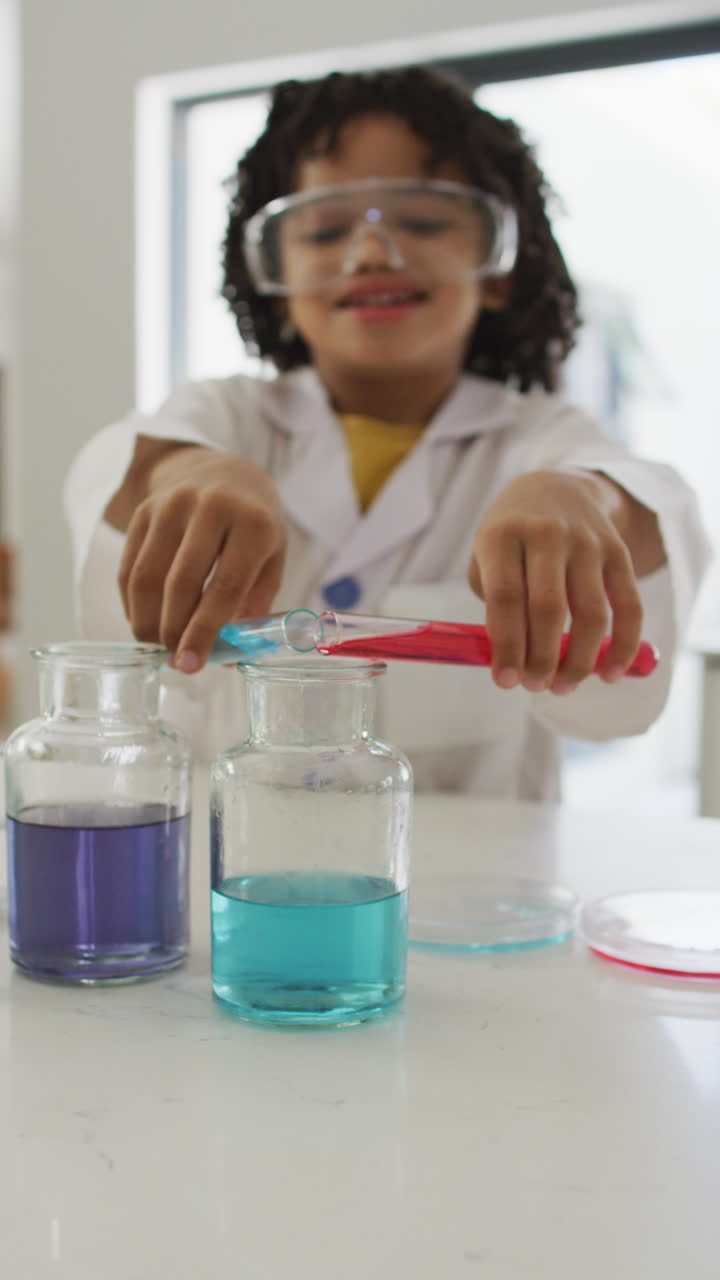 video vertical de un niño biracial feliz haciendo experimentos solo en casa