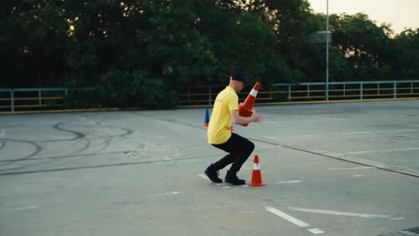 a man in a yellow t-shirt lays out orange cones on the road. motorcycle driver laying out orange cones for student training