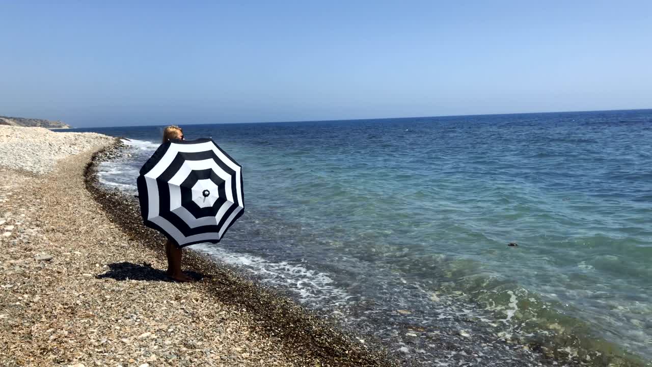 여자 는 바다 의 전망 을 즐기며 손 에 우산을 돌린다