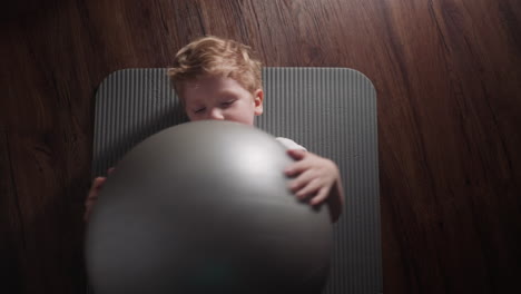 little boy lies on soft mat holding silver gymnastic ball