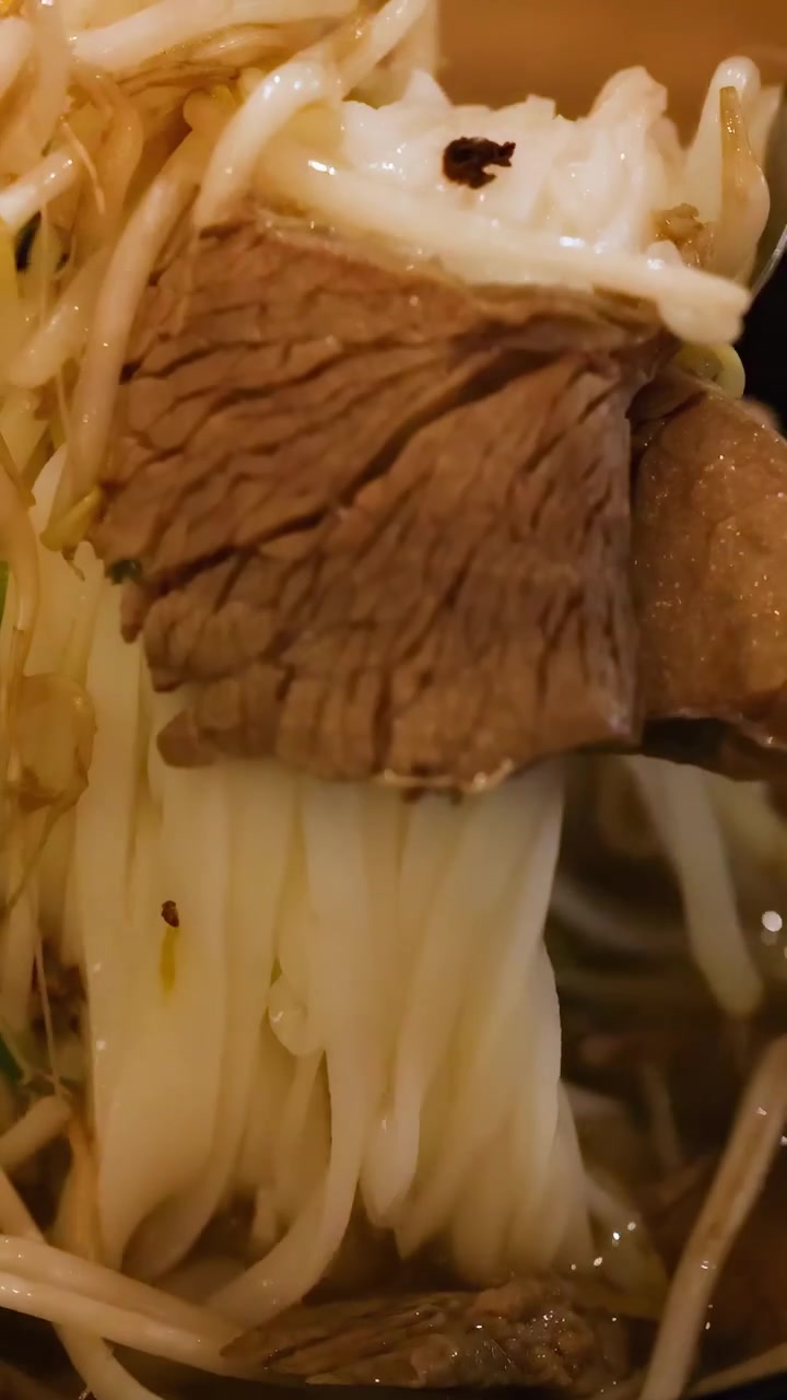 Primi piani di una ciotola fumante di pho vietnamita, che evidenziano noodles, manzo e germogli di soia sotto un'illuminazione calda