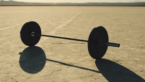 slow motion barbell with weights sitting in empty dry lake bed