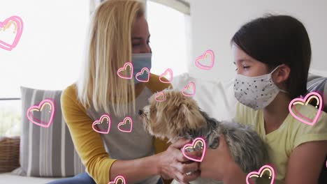 Animation-of-hearts-over-caucasian-woman-and-her-daughter-wearing-face-masks-playing-with-pet-dog