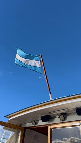 a worn flag waving against a bright sky on a boat in patagonia