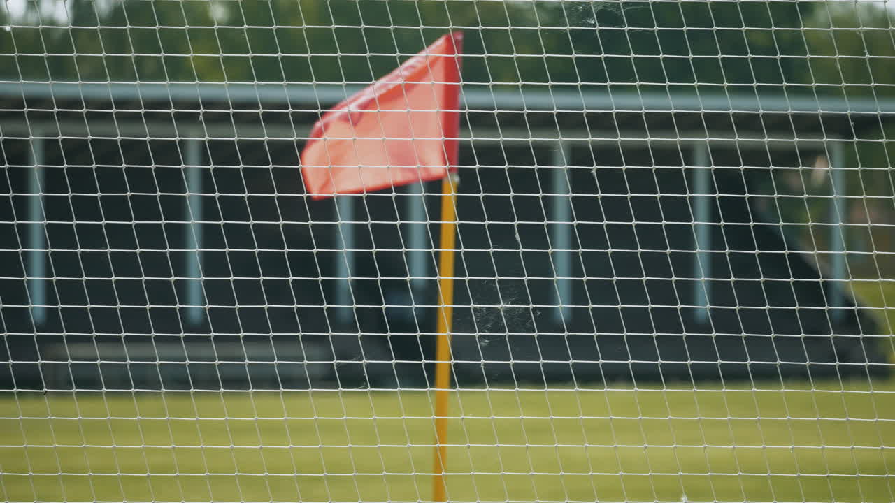 A football, soccer corner flag waving in an empty stadium behind a fence