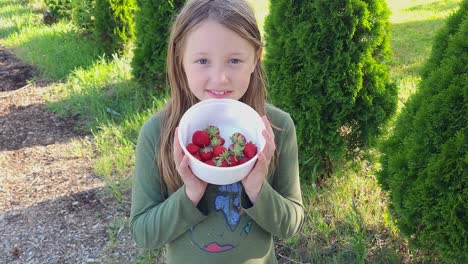 cute young girl holding bowl of strawberry outdoors, sunny warm day