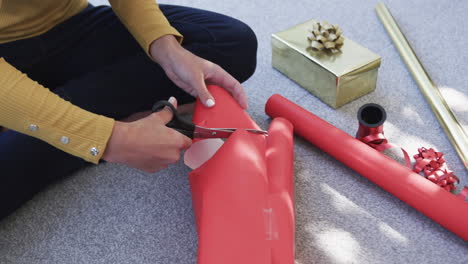 midsection of biracial woman sitting on floor packing christmas presents, slow motion