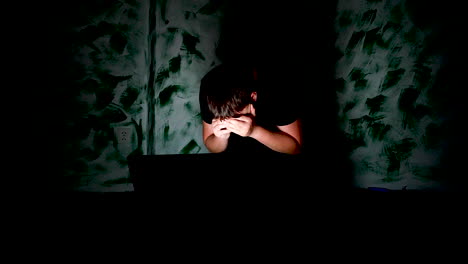 cyberbullying concept, teenager reading hate massages in dark corner of room and covers his face