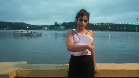 mujer en un traje casual de pie junto a un río con barcos en el fondo al crepúsculo