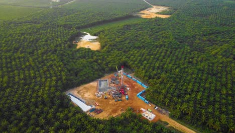 cinematic 4k drone footage of onshore drilling rig equipment structure for oil exploration and exploitation in the middle of jungle surrounded by palm oil trees during sunset and high oil price