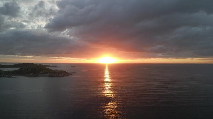 Ripresa aerea panoramica del sole che tramonta sull'orizzonte dell'oceano con il bagliore dorato del sole che luccica sull'acqua