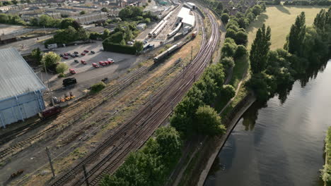 panning aerial drone shot looking down york railway line next to the national railway museum with diesel trains parked at sunset with trees and parked cars