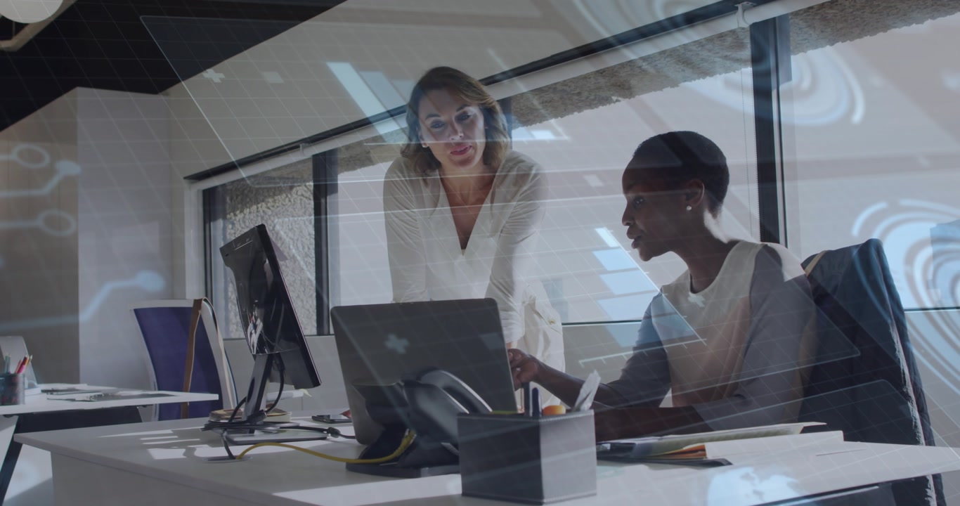 Seated analyst editing data as colleague pointing at screen triggers tech icons guiding review